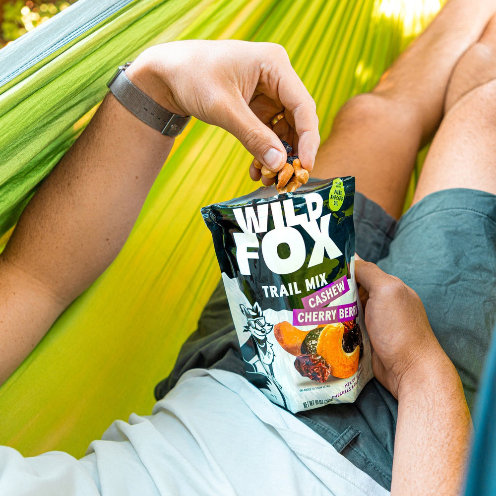 Person holding a Wild Fox Trail Mix packet in a hammock