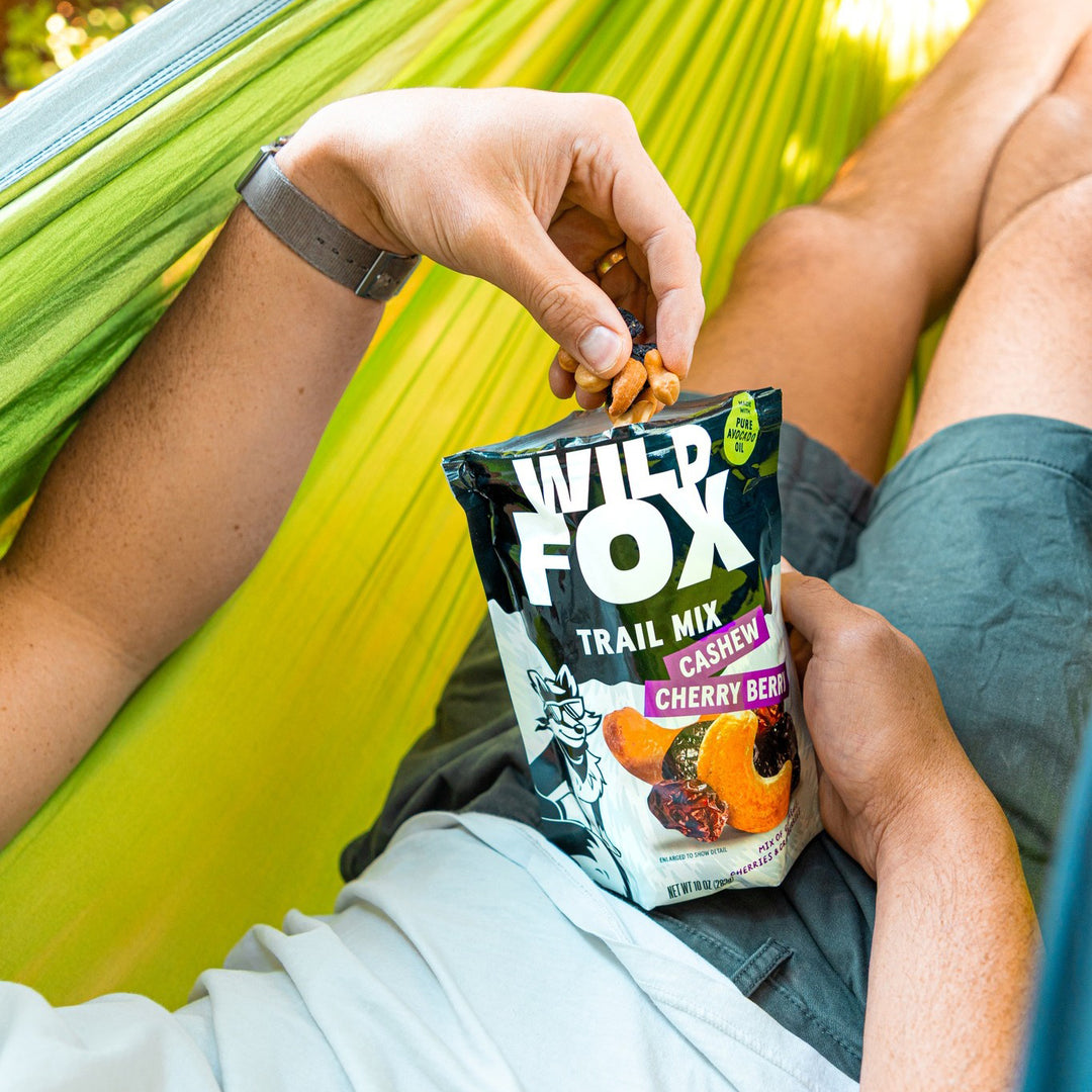 Person holding a Wild Fox Trail Mix packet in a hammock