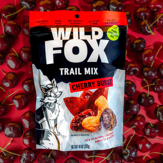 Wild Fox Trail Mix Cherry Burst package surrounded by cherries on a red background