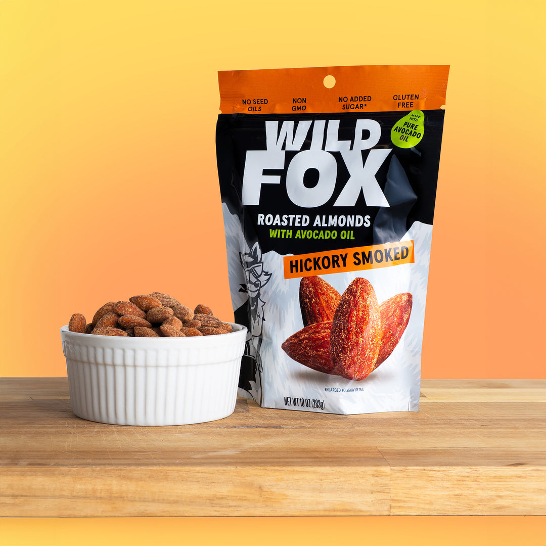 Wild Fox Hickory Smoked Roasted Almonds packaging on a wooden surface with a gradient background