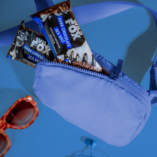 Blue pouch with dark chocolate sea salt Wild Fox protein bars and red sunglasses on a blue background